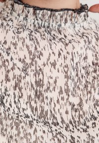 Tissu léger à motifs avec un col à volants. Le design présente des formes abstraites beige et marron avec une texture fine.