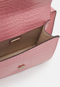 Borsa in ecopelle coccodrillo rosa con texture liscia, chiusura magnetica e interno beige con piccolo motivo ripetuto del marchio.