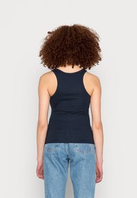 Canotta blu navy con un design aderente, dotata di spalline larghe e una superficie a coste lisce, abbinata a jeans in denim chiaro.