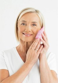 Rosa glassdropperflaske merket "IKKE SPILL" holdt av en person med lys hud, iført en hvit skjorte, smilende og viser et hudpleieprodukt.