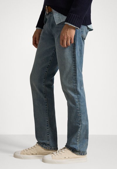 Lyseblå denimjeans med rett benpassform, et brunt lærbelte og beige canvas-sneakers. Uformell stil med en medium vasketekstur.
