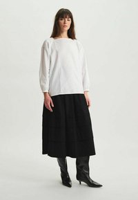 Haut à manches longues blanc avec un décolleté carré, associé à une jupe maxi noire à volants et des bottes noires montantes à talons pointus.