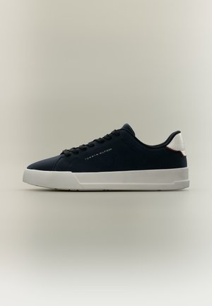 Niedriger schwarzer Sneaker mit weißer Sohle und Fersenzug, schwarzen Schnürsenkeln und kleinem Tommy Hilfiger Logo an der Seite.