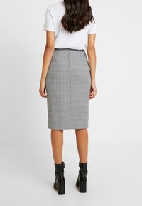 Svartvit houndstooth pennkjol, knälång, slät tyg, centrerad bakseam, bärs med en vit t-shirt och svarta ankellånga stövlar.