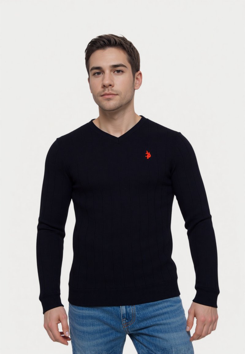 Tengerész csíkos pulóver hosszú ujjal és V-nyakkivágással. A mellkasán egy kis piros logóval. Puha, texturált anyagból készült.