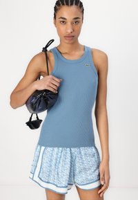Blue ribbed tank top with a small logo, paired with light blue patterned shorts featuring a white trim and a drawstring black bag.