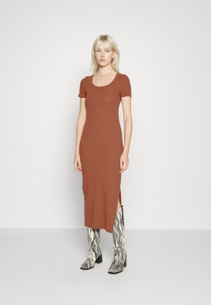 Robe midi ajustée marron avec des manches courtes et des fentes sur les côtés, associée à des bottes noires et blanches marbrées arrivant jusqu'aux genoux. Texture lisse.
