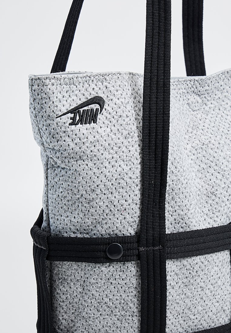 Grau Netz-Tote-Bag mit schwarzen Trägern, ausgestattet mit einem auffälligen schwarzen Nike-Logo, mit einem Druckknopfverschluss, strukturierter Oberfläche und durchdachtem Design.