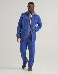 Blue corduroy jacket with multiple pockets and a collared design, paired with matching blue corduroy pants and a light purple hoodie.