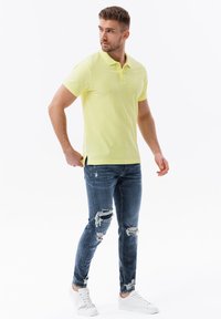 Žluté polo tričko z bavlněné směsi, slim fit, s dvoumístným knoflíkovým zapínáním. Kombinováno s opranými modrými džíny a bílými teniskami.