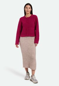 Fuchsia gestrickte Strickjacke mit Rundhalsausschnitt, langen Ärmeln und zwei Vorderaschen, kombiniert mit einem beigen strukturierten Midikleid und grauen Sneakers.