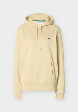 Light beige hooded sweatshirt with front kangaroo pocket, drawstring hood, ribbed cuffs, and small green Lacoste crocodile logo on chest.
