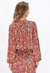 Rode en groene gebloemde blouse met lange, losse mouwen en een gathered halslijn, gemaakt van een gestructureerde, vloeiende stof.