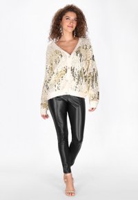 Gouden en zilveren pailletten cardigan met een zachte brei basis, diepe V-hals, en knoopsluiting, gecombineerd met zwarte leren leggings.
