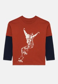 T-shirt à manches longues avec un corps orange, des manches marines et un graphique blanc d'un skateur en action. Fabriqué en coton doux.