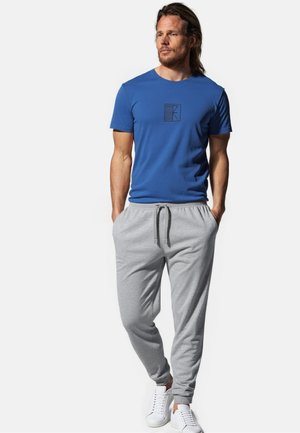 Mandens blå bomulds-t-shirt med et sort logo, parret med lysegrå sweatpants med elastisk talje og ribkant ved anklerne. Hvide sneakers.