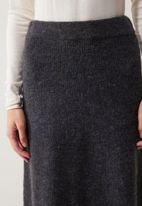 Falda de punto gris oscuro con una textura acanalada y una cinturilla ancha. La tela parece suave y cálida, adecuada para el clima más fresco.