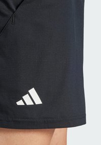 Schwarze Sportshorts aus strukturiertem Stoff, mit einem weißen Adidas-Logo am Saum und dezenten Mustern im Material.