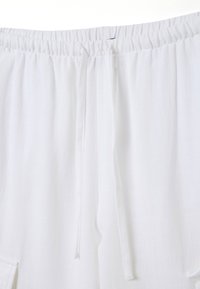 Witte stoffen shorts met een elastische tailleband en trekkoord. Heeft een gestructureerd oppervlak en een zijzak voor gemak.
