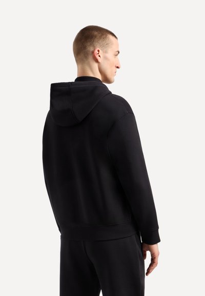 Haut à capuche noir avec une texture douce, présentant une vue de dos, une capuche et une coupe relaxée. Les poignets et l'ourlet sont ajustés pour le confort.