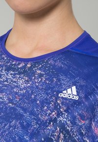 Blue athletic shirt featuring a textured pattern, round neckline, mesh accents on shoulders, and white Adidas logo on the front.