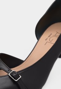 Μαύρο δερμάτινο παπούτσι στυλ Mary Jane με στρογγυλεμένο μύτη, ασημένιο λουράκι με πόρπη και χαμηλό τετράγωνο τακούνι πάνω σε λευκό φόντο.