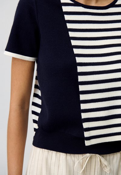 Haut en tricot à rayures bleu marine et blanches à manches courtes avec une coupe décontractée. Présente une section unie bleu marine d'un côté et un motif rayé contrastant.