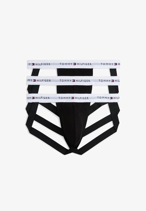Jockstrap negro con tres bandas elásticas blancas marcadas "Tommy Hilfiger" y detalles de tirantes negros adicionales.