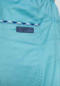 Light blue shorts made of soft fabric, featuring a woven pattern trim on the back pocket and a visible logo label.