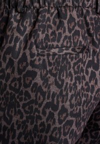 Tissu imprimé léopard en marron foncé et noir. Présente une surface texturée avec un petit détail de poche. Ceinture élastique visible en haut.