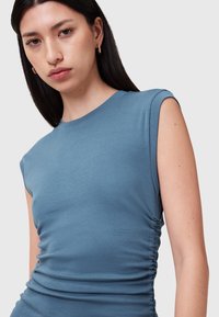 Top blu di manica corta realizzato in morbido tessuto, con dettagli arricciati sui lati e scollatura a girocollo. Tessuto liscio con leggera elasticità.