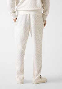 Helle Cremeloungehose mit dezentem Muster, elastischem Bund, Seitentaschen und schmal zulaufenden Beinen. Glatte Textur und lässige Passform.