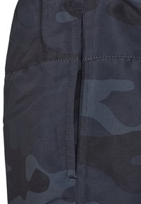 Dunkel getarnte Hose aus strukturiertem Stoff, mit geradem Schnitt und einer seitlichen Reißverschlusstasche mit kontrastierender Naht.