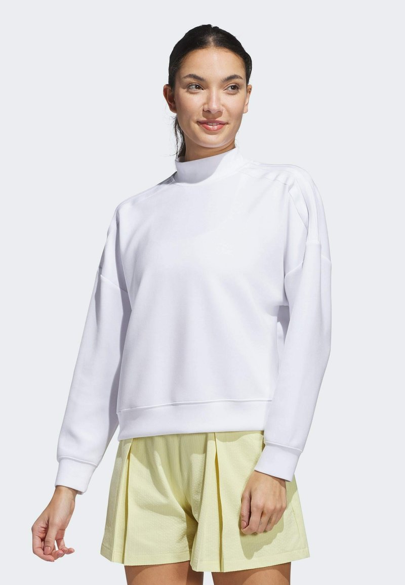 White long-sleeve sweatshirt with a high neck, featuring a relaxed fit and ribbed cuffs. Paired with light yellow pleated shorts.