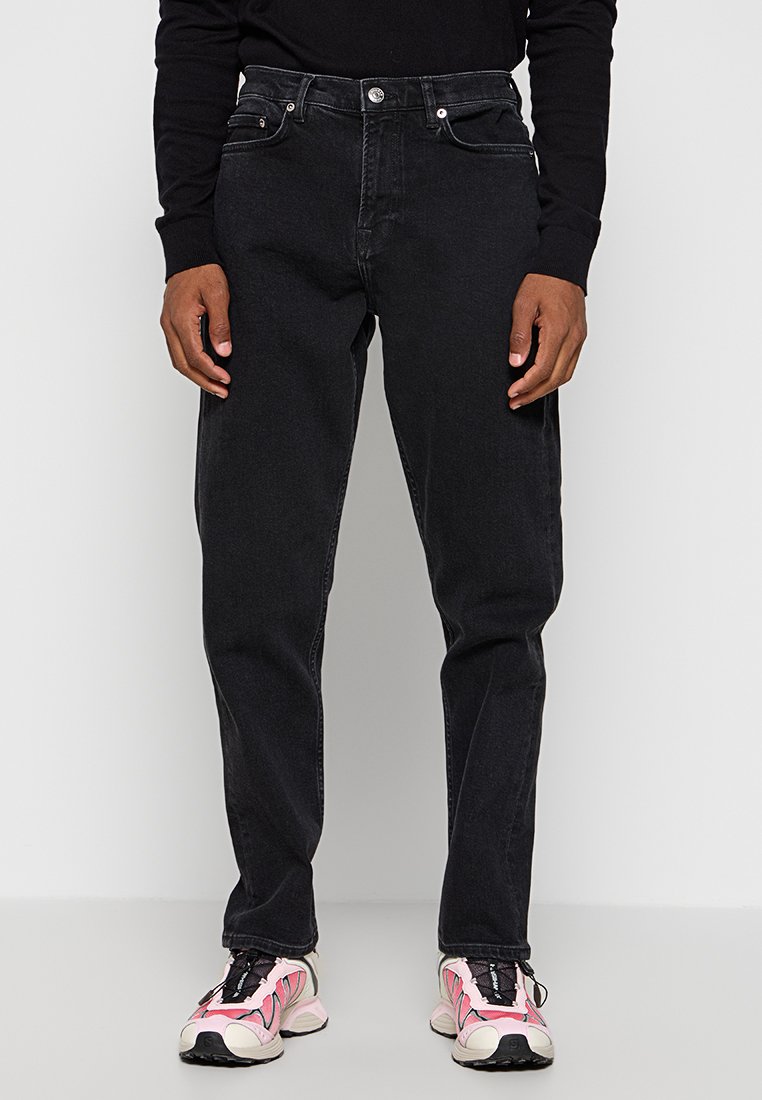 Czarne dżinsy o prostym kroju, z pięcioma kieszeniami i metalowymi elementami. Połączone z różowo-czarnymi sneakersami sportowymi.