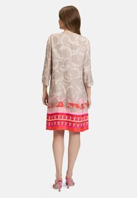 Jasno beżowa sukienka w kwiatowy wzór, z rękawami o długości trzech czwartych i gradientowym dołem w odcieniach różu i czerwieni. Z tyłu dekolt ma małe wycięcie.