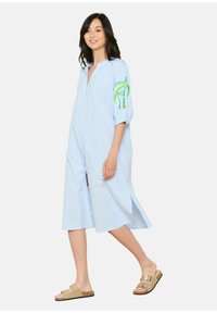Abito button-up a righe blu con maniche a tre quarti, caratterizzato da ricami di palme verdi sulla manica destra e spacchi laterali.
