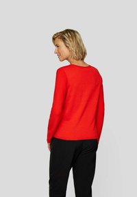 Roter Strickpullover mit gerippter Textur, Rundhalsausschnitt und langen Ärmeln, kombiniert mit schwarzen Hosen, von hinten betrachtet.