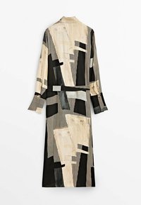 Robe ceinturée à manches longues avec des motifs géométriques abstraits beige, noir et gris sur un tissu à rayures verticales.