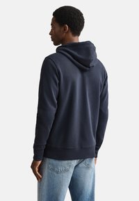 Felpa con cappuccio blu navy con vestibilità comoda, dotata di cappuccio con coulisse e polsini a coste, abbinata a jeans di denim azzurro chiaro.