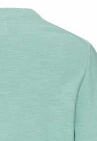 Lichtgroene gebreide stof met een close-up van de achterkant van een kledingstuk, schouder en kraagnaad.