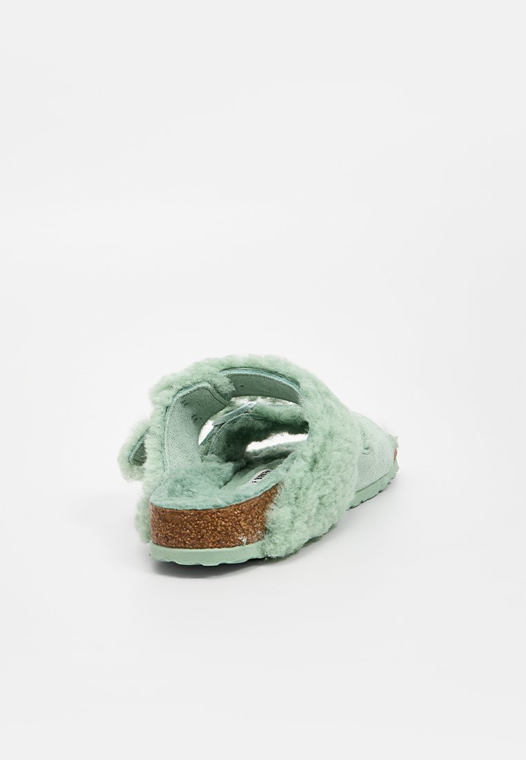 Helle mintgrüne Hausschuhe mit einer flauschigen Textur, offenem Design an der Rückseite, Korksohle und einem weichen Innenfutter. Besitzt einen dezenten Glanz an der Seite.