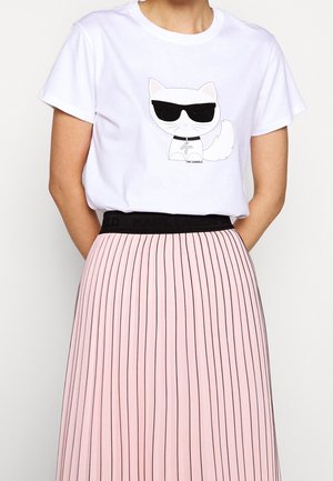 Biała koszulka z krótkim rękawem z nadrukiem kreskówkowego kota w okularach przeciwsłonecznych, zestawiona z różową plisowaną spódnicą w czarne paski.