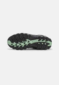 Suela de zapatilla deportiva negra con surcos profundos, con detalles en verde y una superficie texturizada para un mejor agarre. Fabricada con material de goma duradero.