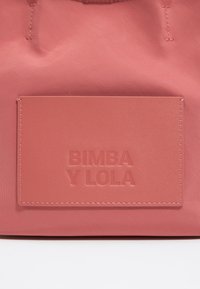 Roza najlonska torba z teksturirano, izbočeno oznako 'BIMBA Y LOLA' in ujemajočim šivanjem za dodaten detajl.