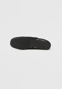 Melnas kurpes ar strukturētu gumijas zoli un acu materiāla augšdaļu, kas piedāvā izgriezumus ventilācijai un komfortam.