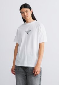 Hvid bomulds t-shirt med rund hals, der har et sort trykt logo, som siger "PORSCHE LEAGUE TURBO CLUB" over et lille Puma-logo.