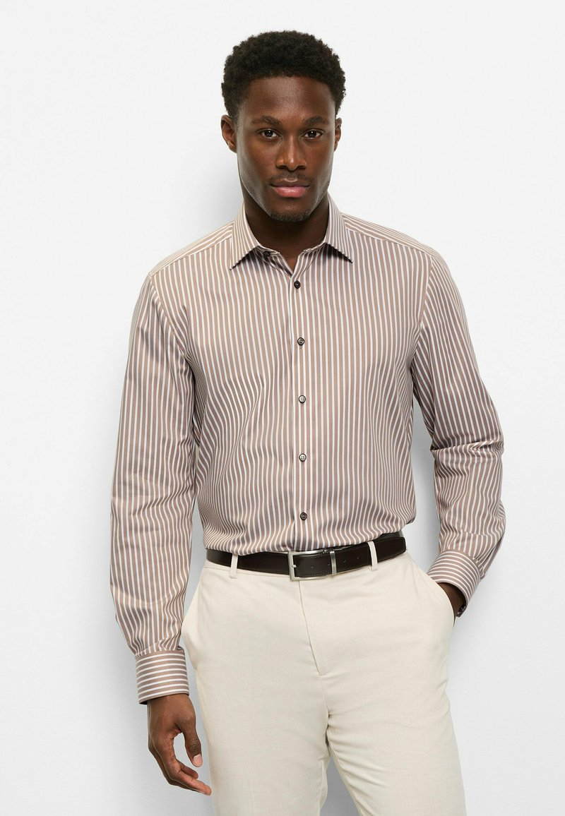 Gestreiftes Hemd mit Knöpfen in Braun und Creme, mit langen Ärmeln, Kragen und schwarzen Knöpfen, kombiniert mit hellen Hosen.