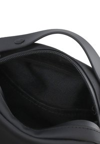 Borsa nera con una superficie liscia, dotata di chiusura con zip e foderatura interna nera. Include un manico arrotondato sopra.