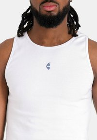 Top in cotone bianco a coste con un logo ricamato blu sottile sulla zona sinistra del petto. Tessuto liscio con un design senza maniche classico.